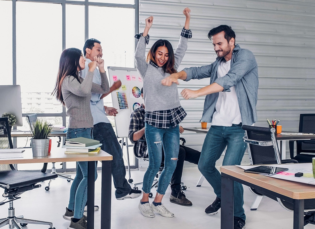 Insurance Solutions - Group of Colleagues Cheer and Dance by Their Work Stations in an Office