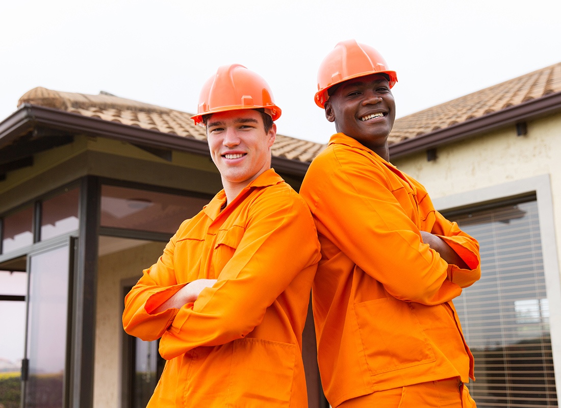 Insurance by Industry - Two Contractors Stand Back to Back in Their Orange Uniforms While Working at a House